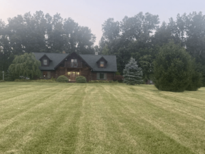 A large two-story home behind a large front yard, nestled between tall trees.