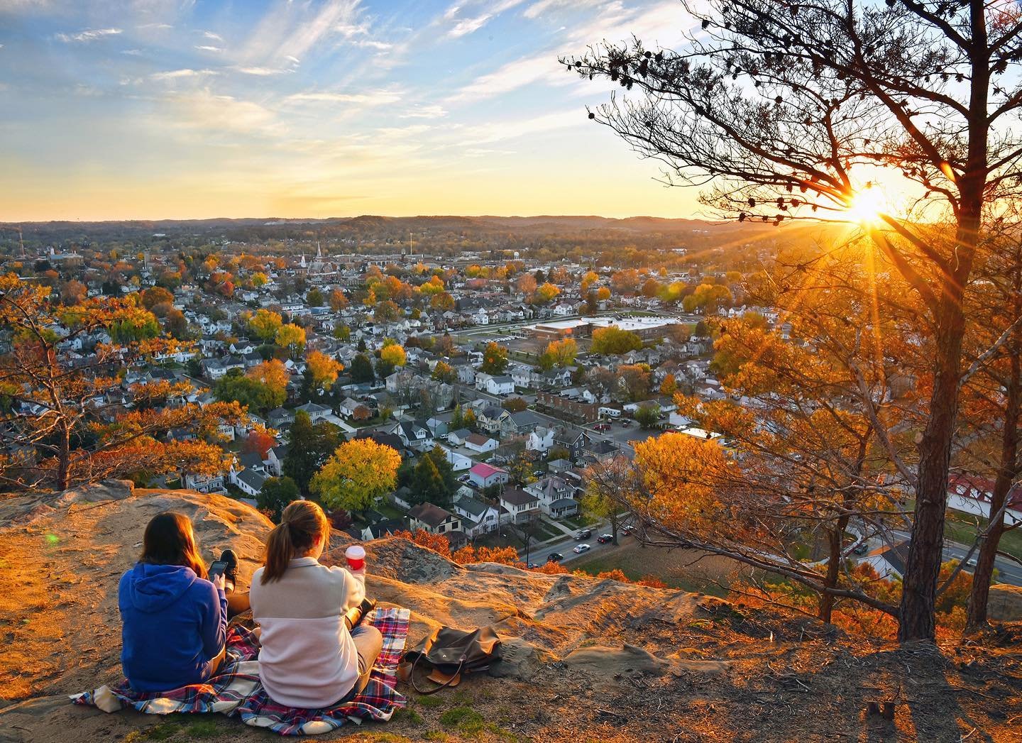 Two women enjoying the view from a checkered picnic blanket on Mount Pleasant overlooking a town.