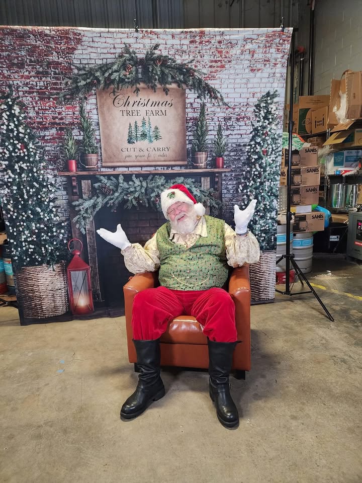 Photo of Santa in front of a fireplace and christmas tree display